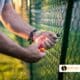 A man does fence repair maintenance on a black chain link fence.