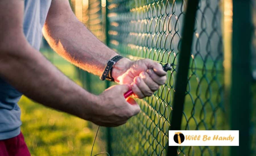 A man does fence repair maintenance on a black chain link fence.