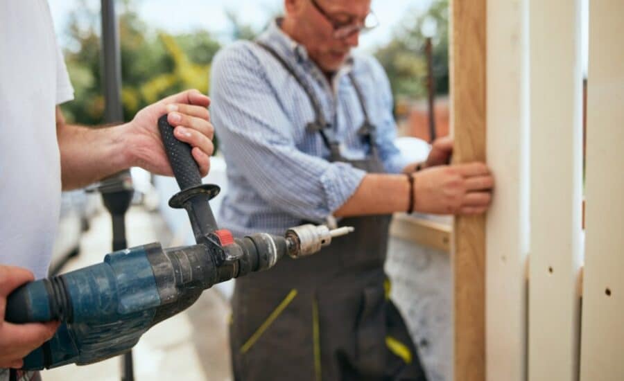 A handyman in Hampstead, NC, uses a drill to construct a wooden fence, showcasing his skills in home improvement.